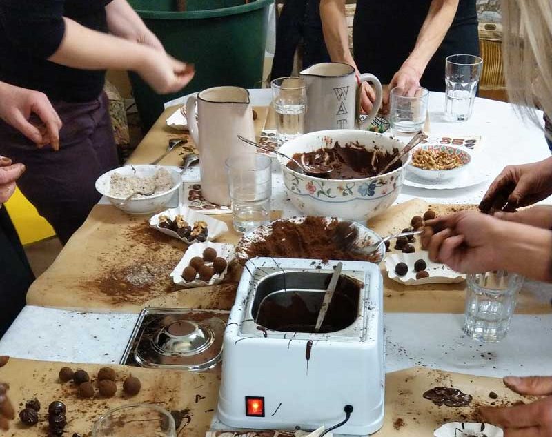 Leute bereiten gemeinsam Pralinen zu, Hände und Zutaten sind überall verstreut.