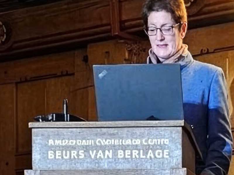 Eine Person spricht am Rednerpult während einer Präsentation. Laptop ist geöffnet.