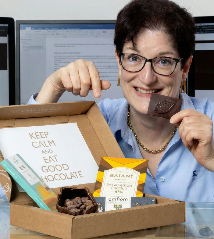 Frau mit Brille deutet auf eine Schachtel Schokoladen und zeigt auf eine Karte mit „Keep calm and eat good chocolate“.