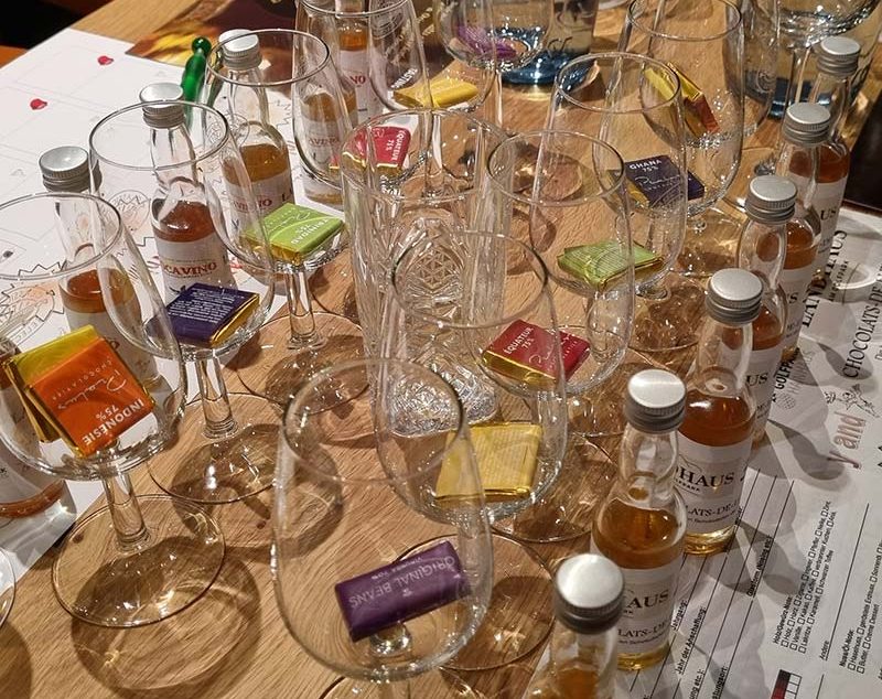 Tisch mit Gläsern und Schokoladen, umgeben von verschiedenen kleinen Whisky Flaschen