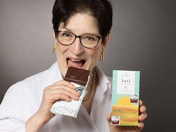 Michaela Schupp hält eine Tafel Schokolade und lächelt, während sie einen Bissen nimmt.